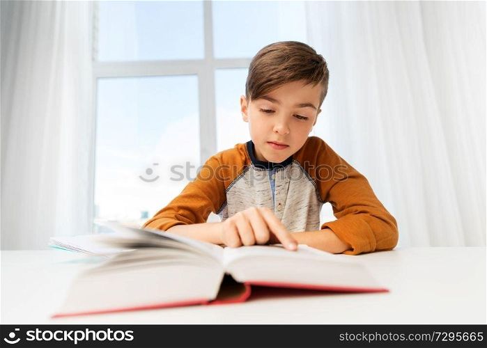 education, childhood and people concept - student boy reading book at home. student boy reading book at home table