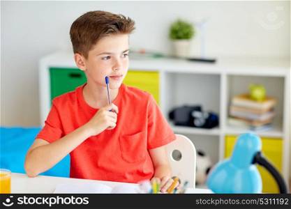 education, childhood and people concept - student boy with pen and notebook thinking at home. student boy with pen and notebook thinking at home