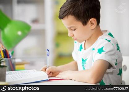 education, childhood and school concept - close up of boy with textbook writing to notebook at home. close up of boy with textbook writing at home