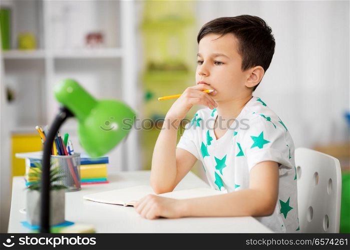 education, childhood and school concept - little boy sitting at desk and writing to notebook at home. little boy writing to notebook at home