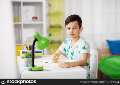 education, childhood and school concept - little boy sitting at desk and writing to notebook at home. little boy writing to notebook at home