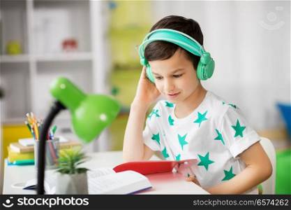 education, childhood and school concept - student boy in headphones reading book at home. student boy in headphones reading book at home
