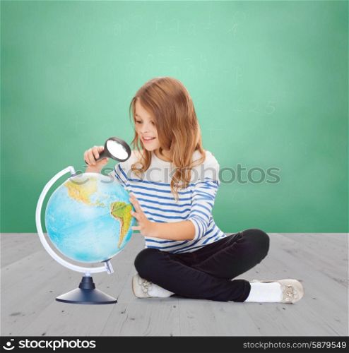 education, childhood, geography and school subject concept - happy little student girl looking at globe with magnifier over green chalk board background