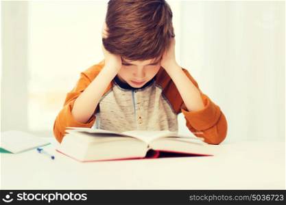 education, childhood, people, homework and school concept - bored or displeased student boy reading book or textbook at home. student boy reading book or textbook at home