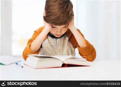 education, childhood, people, homework and school concept - bored or displeased student boy reading book or textbook at home