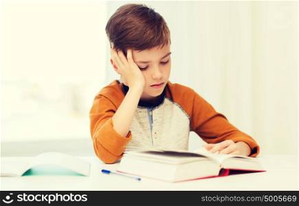 education, childhood, people, homework and school concept - bored student boy reading book or textbook at home. student boy reading book or textbook at home