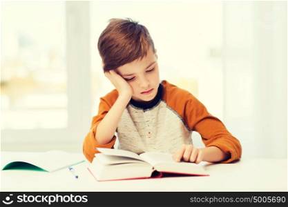 education, childhood, people, homework and school concept - bored student boy reading book or textbook at home. student boy reading book or textbook at home