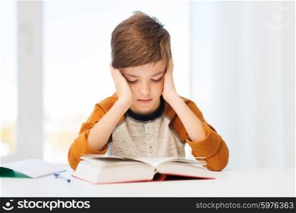 education, childhood, people, homework and school concept - bored student boy reading book or textbook at home