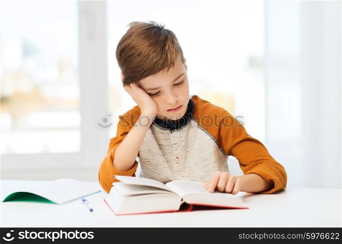 education, childhood, people, homework and school concept - bored student boy reading book or textbook at home