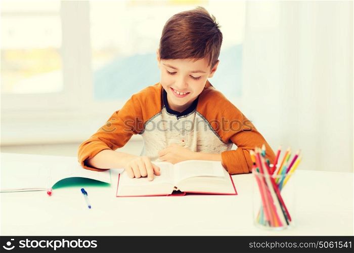 education, childhood, people, homework and school concept - happy student boy reading book or textbook at home. smiling, student boy reading book at home