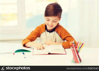 education, childhood, people, homework and school concept - happy student boy reading book or textbook at home. smiling, student boy reading book at home