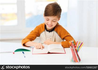 education, childhood, people, homework and school concept - happy student boy reading book or textbook at home