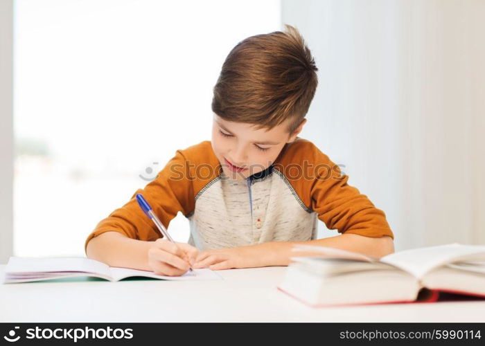 education, childhood, people, homework and school concept - smiling student boy with book writing to notebook at home