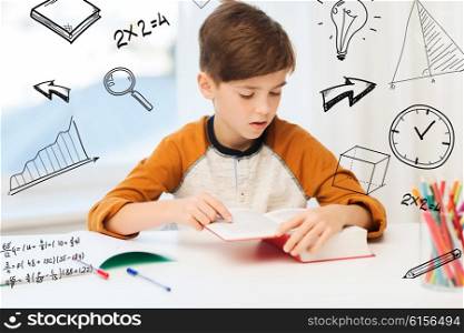 education, childhood, people, homework and school concept - student boy reading book or textbook at home over mathematical doodles