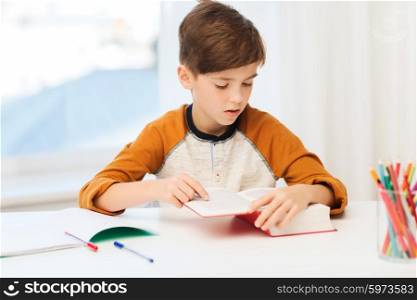 education, childhood, people, homework and school concept - student boy reading book or textbook at home