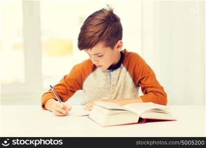 education, childhood, people, homework and school concept - student boy with book writing to notebook at home. student boy with book writing to notebook at home