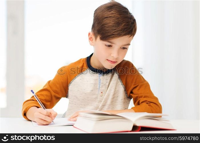 education, childhood, people, homework and school concept - student boy with book writing to notebook at home