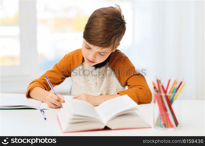 education, childhood, people, homework and school concept - student boy with book writing to notebook at home
