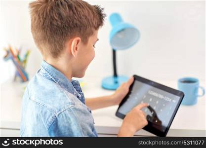 education, childhood, technology and people concept - smiling student boy using calculator on tablet pc computer and counting at home. student boy counting on tablet pc calculator