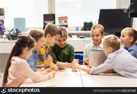 education, children, technology, science and people concept - group of happy kids with laptop computer building robots at robotics school lesson