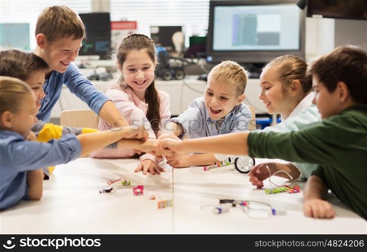 education, children, technology, science and people concept - group of happy kids building robots at robotics lesson and making fist bump