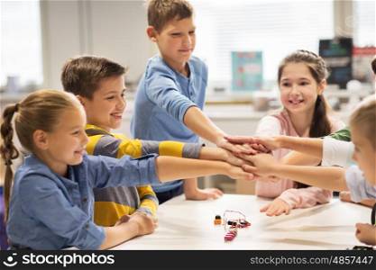 education, children, technology, science and people concept - group of happy kids building robots l at robotics lesson and holding hands together