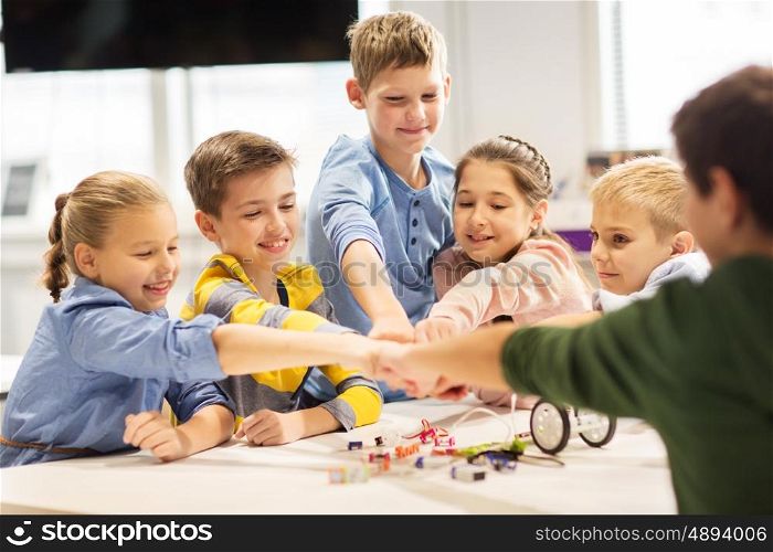 education, children, technology, science and people concept - group of happy kids building robots at robotics lesson and making fist bump