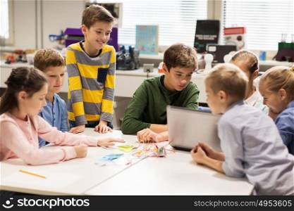 education, children, technology, science and people concept - group of happy kids with laptop computer building robots at robotics school lesson. happy children with laptop at robotics school
