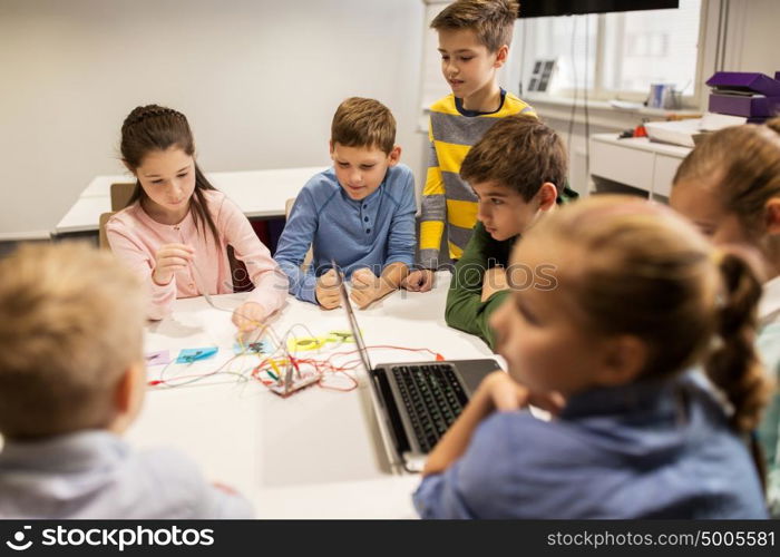 education, children, technology, science and people concept - group of happy kids with laptop computer playing and invention kit at robotics school lesson. kids with invention kit at robotics school