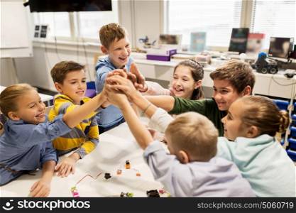 education, children, technology, science and people concept - group of happy kids building robots and making high five gesture at robotics school. happy children making high five at robotics school