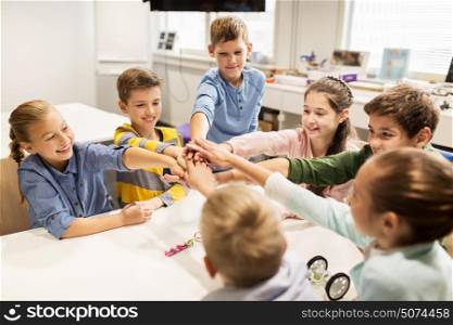 education, children, technology, science and people concept - group of happy kids building robots l at robotics lesson and holding hands together. happy children holding hands at robotics school