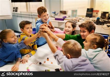 education, children, technology, science and people concept - group of happy kids building robots and making high five gesture at robotics school. happy children making high five at robotics school