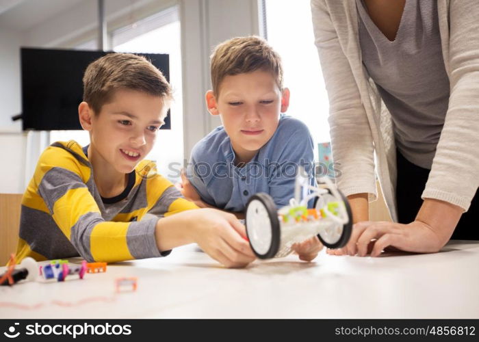 education, children, technology, science and people concept - happy boys and teacher building robot at robotics school lesson