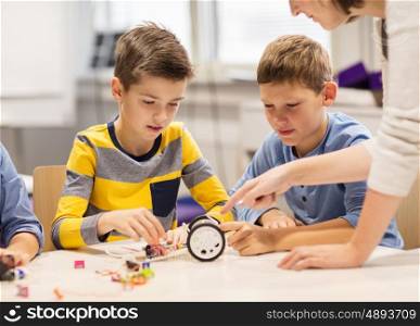 education, children, technology, science and people concept - happy boys and teacher building robot at robotics school lesson