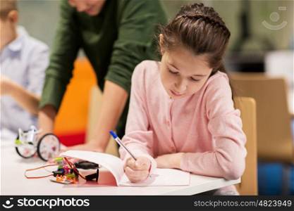education, children, technology, science and people concept - happy girl writing to notebook at robotics school