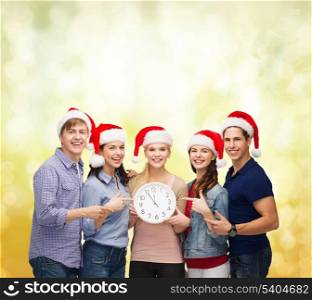 education, christmas, happiness and people concept - group of smiling students in santa helper hats with clock showing 12