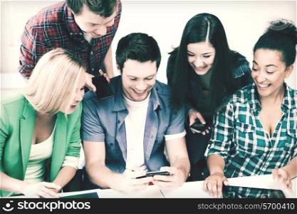 education concept - group of students looking into smartphone at school