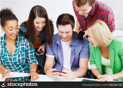 education concept - group of students looking into smartphone at school