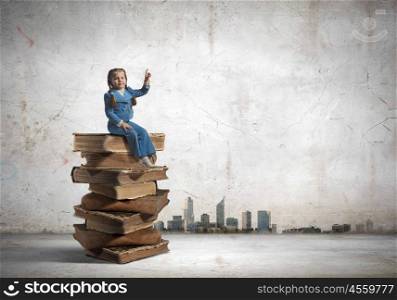 Education concept. Image of cute school girl in sitting on pile of books
