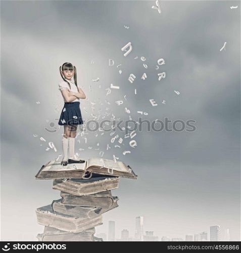 Education concept. Image of cute school girl standing on pile of books