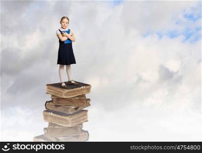 Education concept. Image of cute school girl standing on pile of books