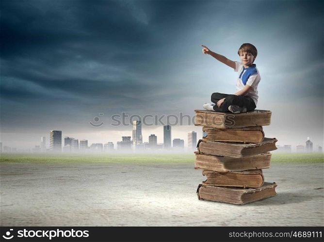 Education concept. Image of little cute boy sitting on pile of books
