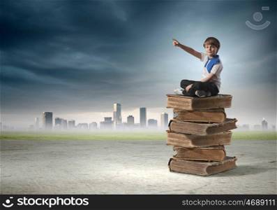 Education concept. Image of little cute boy sitting on pile of books