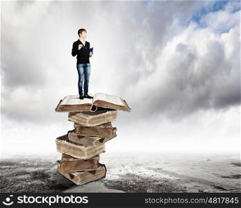 Education concept. Image of little cute boy standing on pile of books
