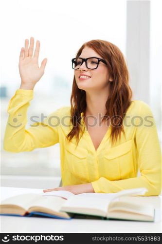 education concept - smiling student girl in eyeglasses with books and raised hand in college