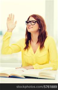 education concept - smiling student girl in eyeglasses with books and raised hand in college