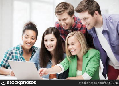 education concept - smiling students looking at laptop at school