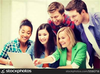 education concept - smiling students looking at laptop at school