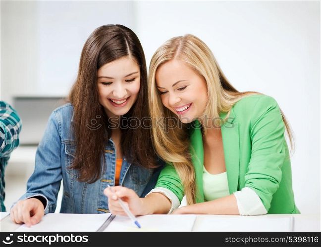 education concept - student girls pointing at notebook at school