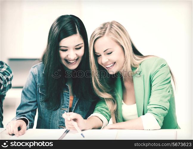 education concept - student girls pointing at notebook at school